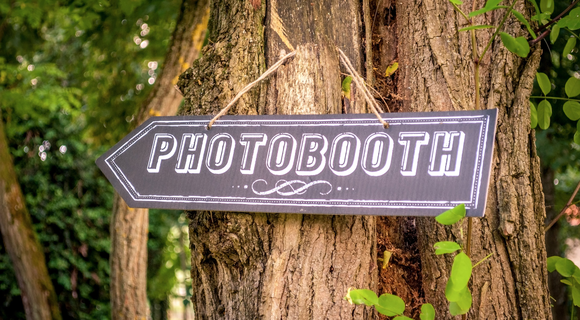 Pancarte accrochée à un arbre indiquant la direction du photo booth de mariage
