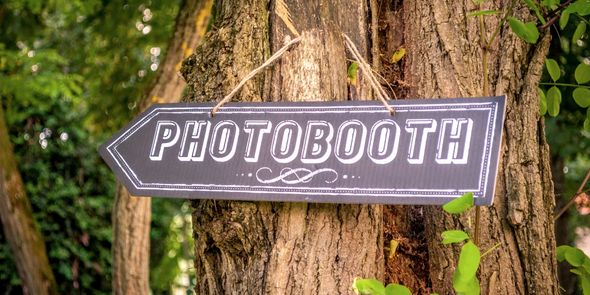 Pancarte accrochée à un arbre indiquant la direction du photo booth de mariage