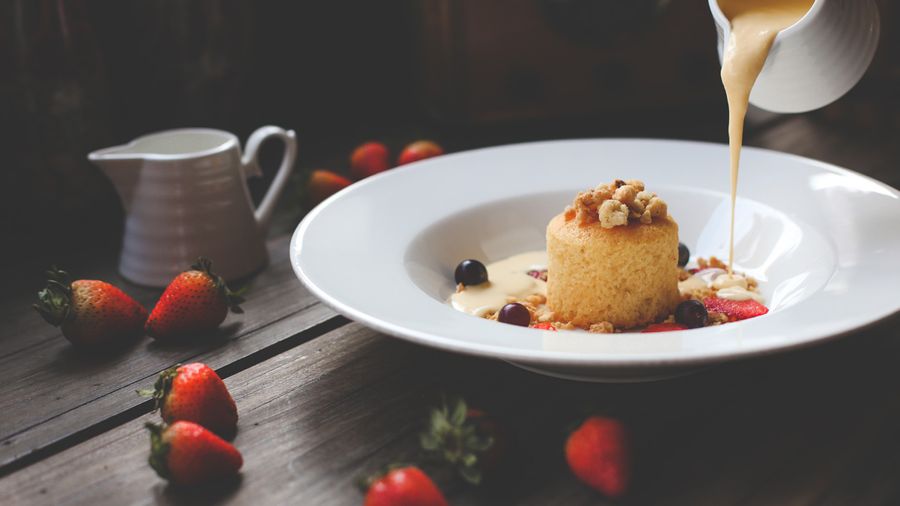 Photographie culinaire d'un dessert avec crème anglaise versée, joliment mise en scène