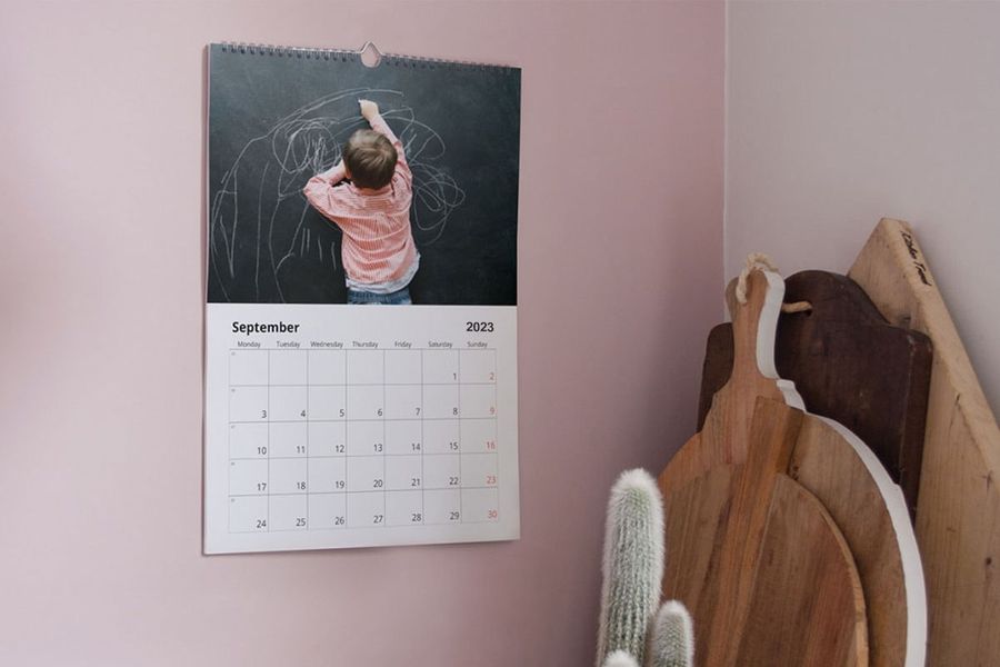 Image d'un calendrier photo sur un mur rose montrant un petit garçon en train de dessiner sur un tableau noir.