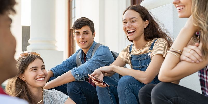 Un groupe d’étudiants souriants assis ensemble, pour inspirer Photobox et des idées de cadeaux de remise de diplôme ainsi qu’un yearbook universitaire personnalisé.