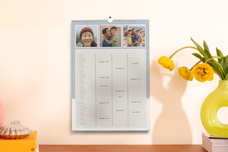 Un planificateur familial est accroché au mur à côté d'un vase et de quelques livres, illustrant le conseil de Photobox pour rester organisé pendant l'année scolaire grâce à un planificateur personnalisé.