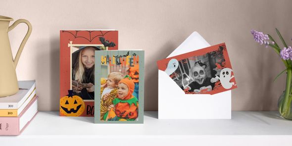 Trois cartes personnalisées pour Halloween sont alignées sur une cheminée, représentant une petite fille déguisée en sorcière, un petit garçon déguisé en citrouille et une petite fille déguisée en fantôme entourée d'illustrations de fantômes, présentant le guide de Photobox pour créer des invitations d'Halloween réussies.