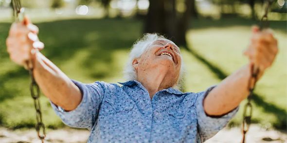 Un homme âgé souriant sur une balançoire en extérieur lors d’une belle journée de printemps ensoleillée, pour inspirer Photobox et des idées de photos de printemps à capturer pendant la saison printanière.