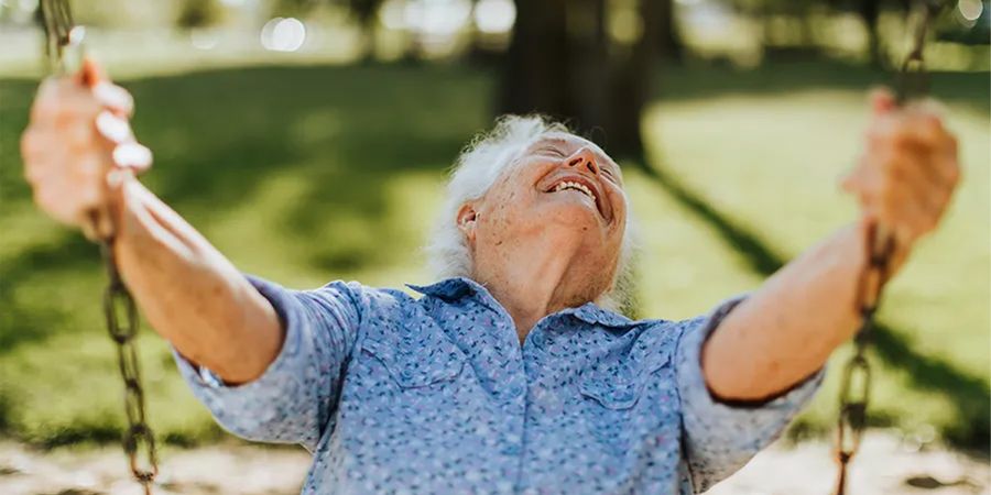 Un homme âgé souriant sur une balançoire en extérieur lors d’une belle journée de printemps ensoleillée, pour inspirer Photobox et des idées de photos de printemps à capturer pendant la saison printanière.