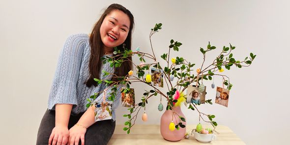 Vannie, spécialiste marketing social chez Photobox, à côté d un centre de table de Pâques DIY terminé, composé d un arbre dans un vase avec des tirages photo personnalisés accrochés aux branches.