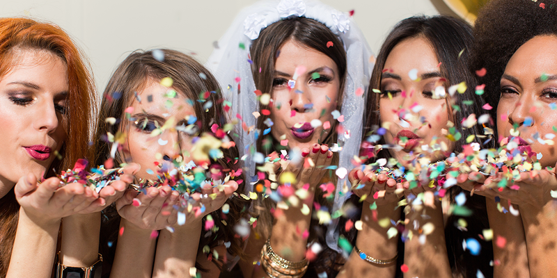 Une femme avec un voile soufflant des confettis avec quatre amies, trouvant des idées pour un enterrement de vie de jeune fille avec Photobox.