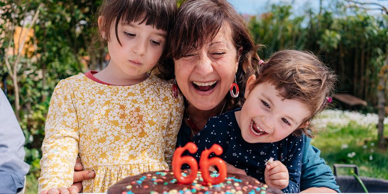 Une femme sourit près de son gâteau d'anniversaire orné de bougies indiquant « 66 », entourée d'une jeune fille et d'un jeune garçon, présentant le guide ultime des cadeaux d'anniversaire de Photobox.