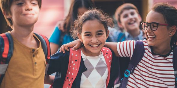 Trois amis d'école s'enlacent et sourient à l'objectif, capturant la joie de la rentrée scolaire dans le guide de Photobox pour de belles photos de rentrée.