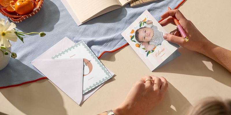 Une femme rédigeant un texte pour faire part naissance pour une petite fille sur une carte personnalisée de Photobox.