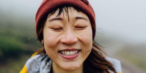 Femme souriante les yeux fermés, portant une tenue d’hiver et un bonnet rouge en extérieur, pour illustrer les 75 idées de légendes photo d’automne de Photobox pour Instagram.