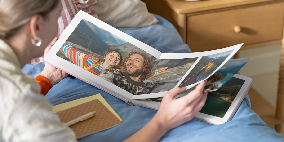 Inspiration livre photo Photobox : une femme regarde un livre photo personnalisé ouvert montrant une double page avec un couple dans un paysage montagneux.