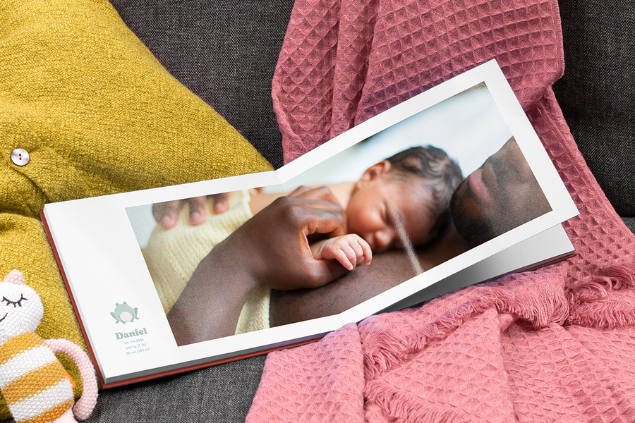 Un père tenant son nouveau-né dans un livre photo ma première année ouvert présentant les statistiques de naissance du bébé.