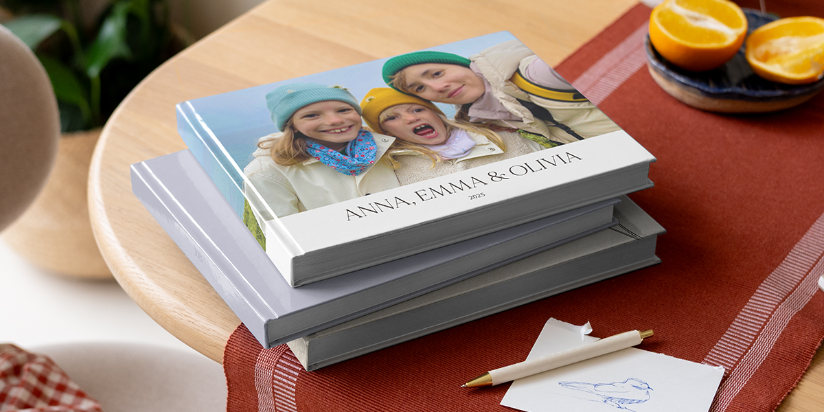 Une sélection de livres photo Photobox avec un stylo, montrant des frères et sœurs sur la couverture pour trouver une phrase pour album photo famille ou une phrase d'accroche album photo.