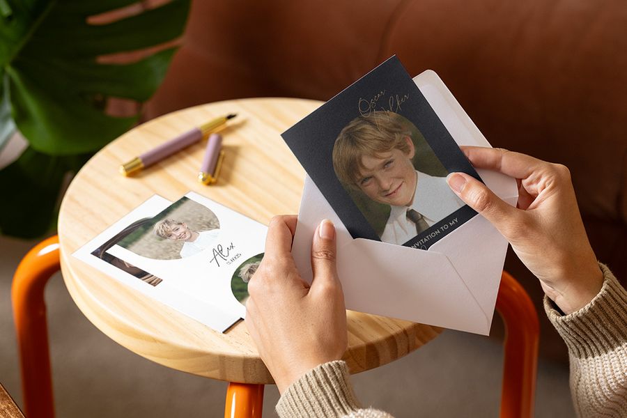 Une personne regarde des invitations de première communion pour garçon de chez Photobox, avec d'autres invitations disposées sur une table en arrière-plan.