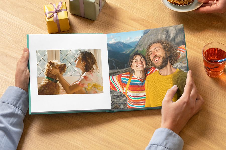 Un livre photo anniversaire à couverture rigide Photobox ouvert, montrant une femme avec son chien et un couple souriant en voyage, idéal comme livre photo personnalisé anniversaire.