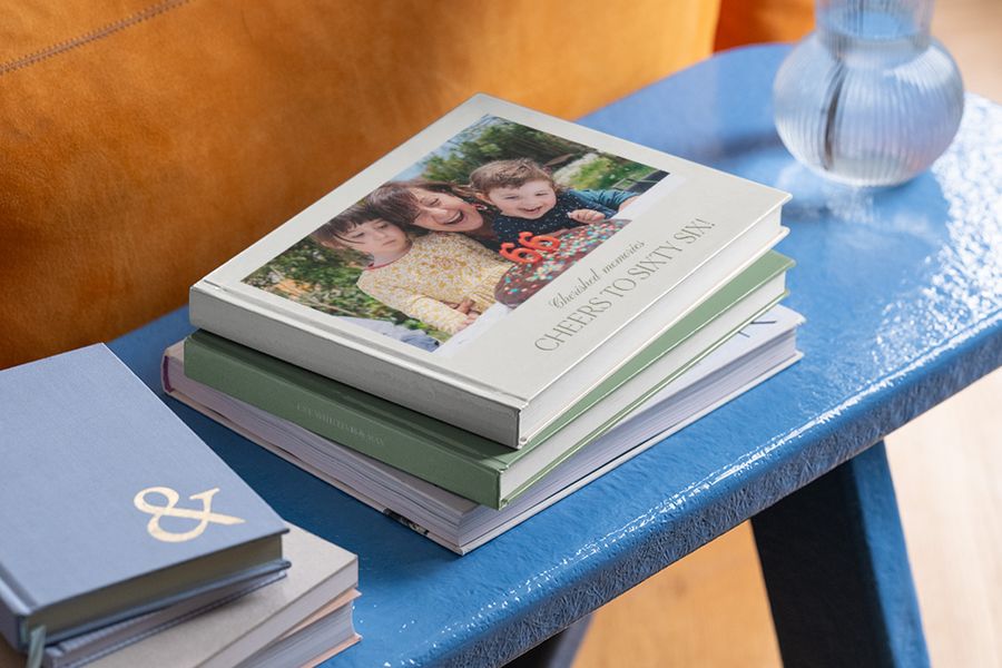 Une pile de livre photo anniversaire sur une table, celui du dessus montre une grand-mère et ses petits-enfants, parfait comme livre photo personnalisé anniversaire chez Photobox.