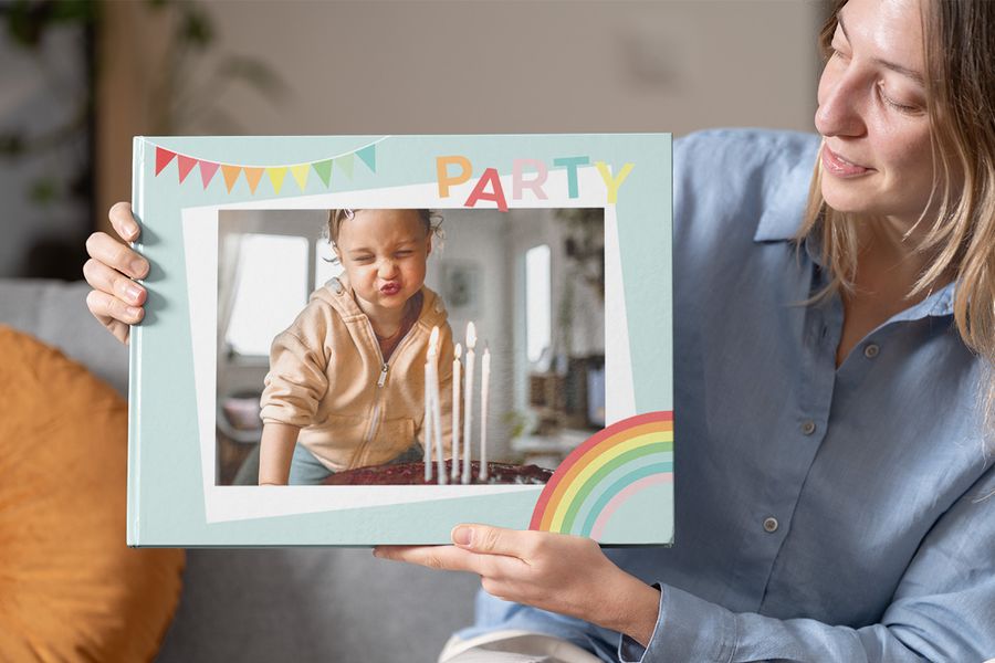 Une femme tient un livre photo anniversaire Photobox sur le thème de la fête avec un enfant soufflant ses bougies, parfait pour faire un livre photo pour un anniversaire.