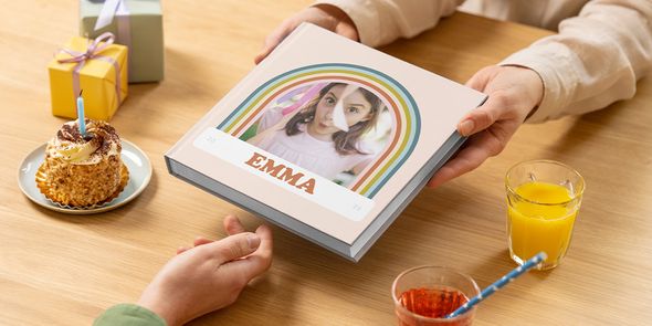 Un livre photo anniversaire pour Emma est passé sur une table avec un gâteau et un cadeau, illustrant un livre photo pour anniversaire ou un livre photo personnalisé anniversaire avec Photobox.