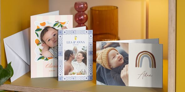 Une sélection de cartes personnalisées sur une étagère, incluant deux faire-part de naissance et un de mariage, illustrant la facilité de création avec Photobox.