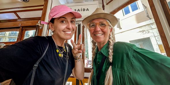 Une mère et sa fille adulte souriantes assises dans un tramway, la fille faisant un signe de paix, illustrant des idées de cadeau fete des meres et de messages de vœux avec Photobox.