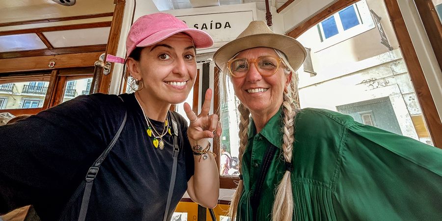 Une mère et sa fille adulte souriantes assises dans un tramway, la fille faisant un signe de paix, illustrant des idées de cadeau fete des meres et de messages de vœux avec Photobox.