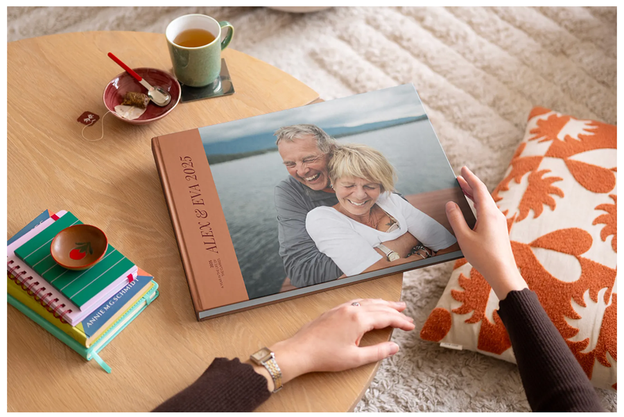 Quelqu'un s'apprête à ouvrir un livre photo personnalisé premium layflat 2025 sur une table basse, avec un couple de seniors souriants en couverture chez Photobox.