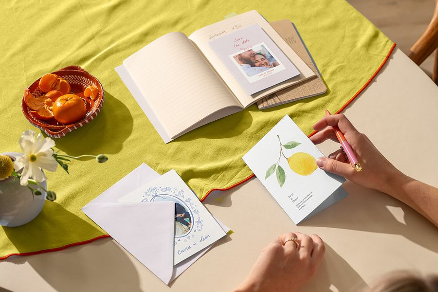 Une collection de faire-part de mariage tendance sur une nappe aux couleurs d'agrumes, illustrant les tendances mariage 2026 et comment choisir le thème de couleur avec Photobox.