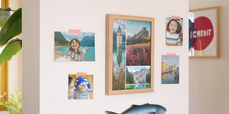 Des tirages photo Photobox exposés sur un mur dans une maison, avec un grand cadre rempli de photos de paysages et quatre tirages photo de famille individuels, pour inspirer le tirage photo et des idées d’impression photo en ligne.