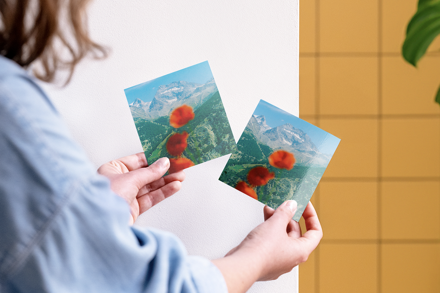 Une femme compare deux tirages photo Photobox de la même photo de paysage de montagne avec des fleurs au premier plan, montrant un tirage photo mat et un tirage photo brillant pour aider à choisir la bonne finition pour le tirage photo.