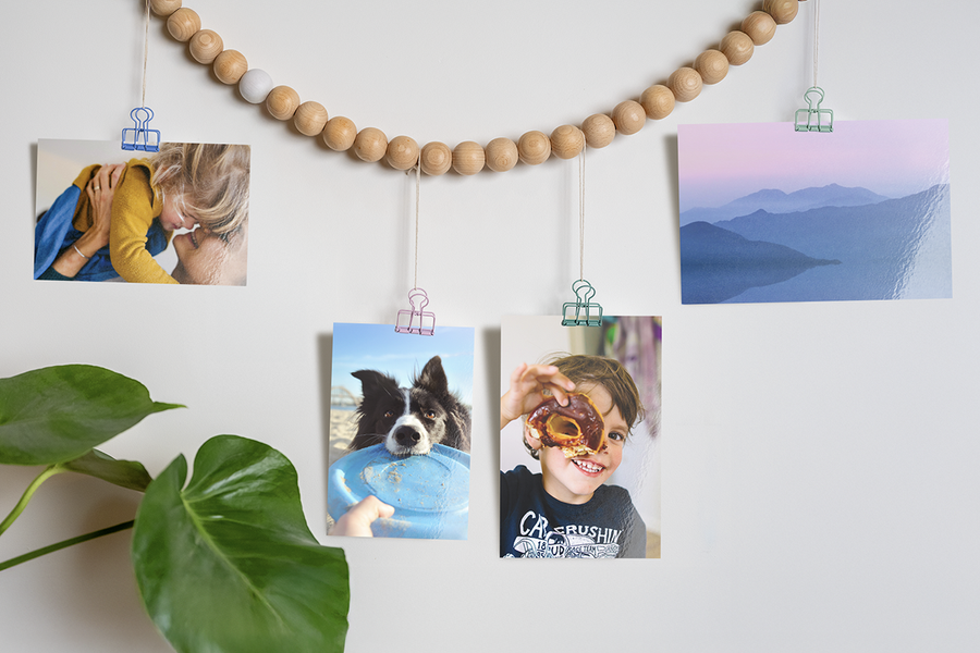 Idées créatives pour exposer des tirages photo Photobox, avec des photos de famille représentant un chien, un enfant avec un donut et un paysage suspendues à une guirlande perlée avec des clips, pour inspirer le tirage photo et des idées d’impression photo en ligne.