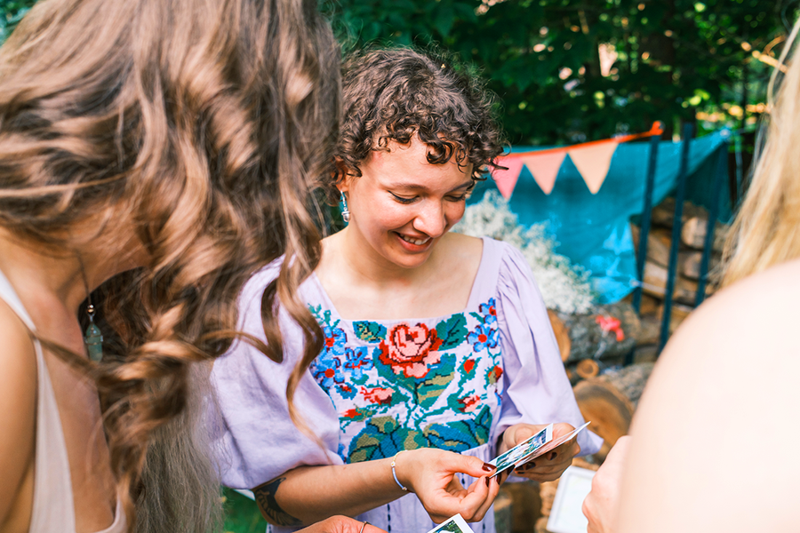 Une femme en tenue élégante lors d’un mariage tient des tirages photo pour un jeu de mission secrète, pour inspirer Photobox et des jeux mariage pour les invités.