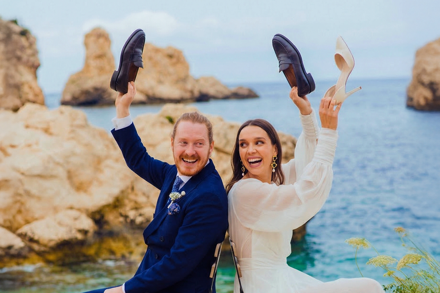 Une mariée et un marié sur la plage le jour de leur mariage jouent au jeu des chaussures, pour inspirer Photobox et des jeux mariage pour animer un mariage.