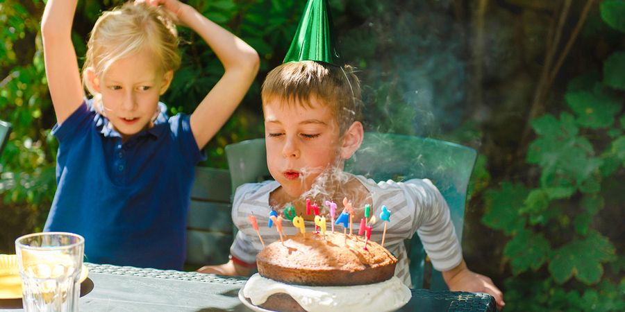 Un garçon souffle les bougies de son gâteau d’anniversaire, pour inspirer Photobox et une fête d’anniversaire enfant inoubliable.