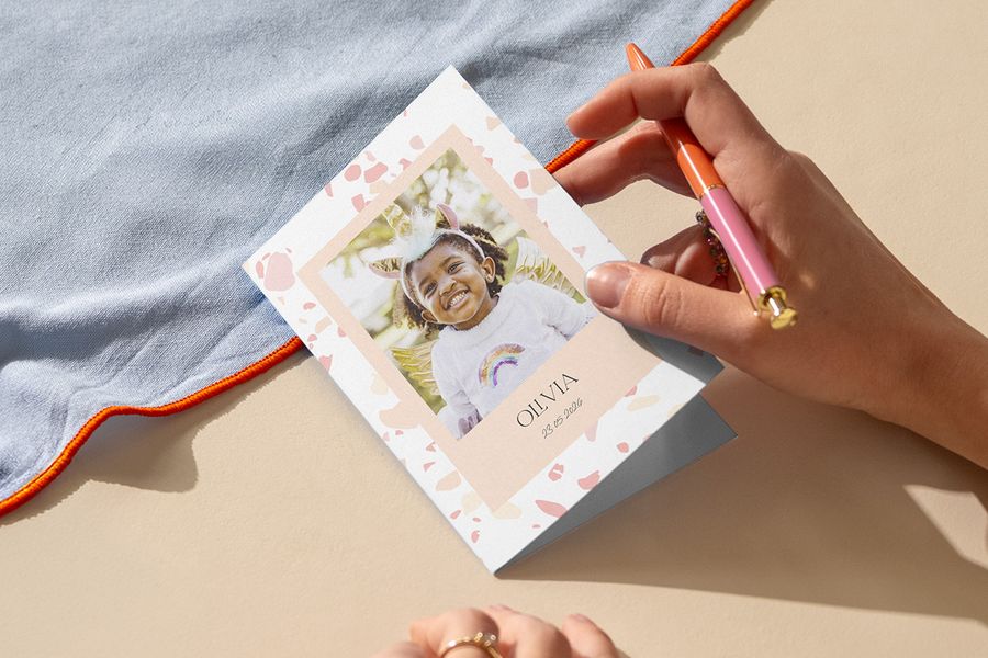 Une personne écrit une invitation pour l’anniversaire d’un enfant, pour inspirer Photobox et une invitation goûter d’anniversaire personnalisée.