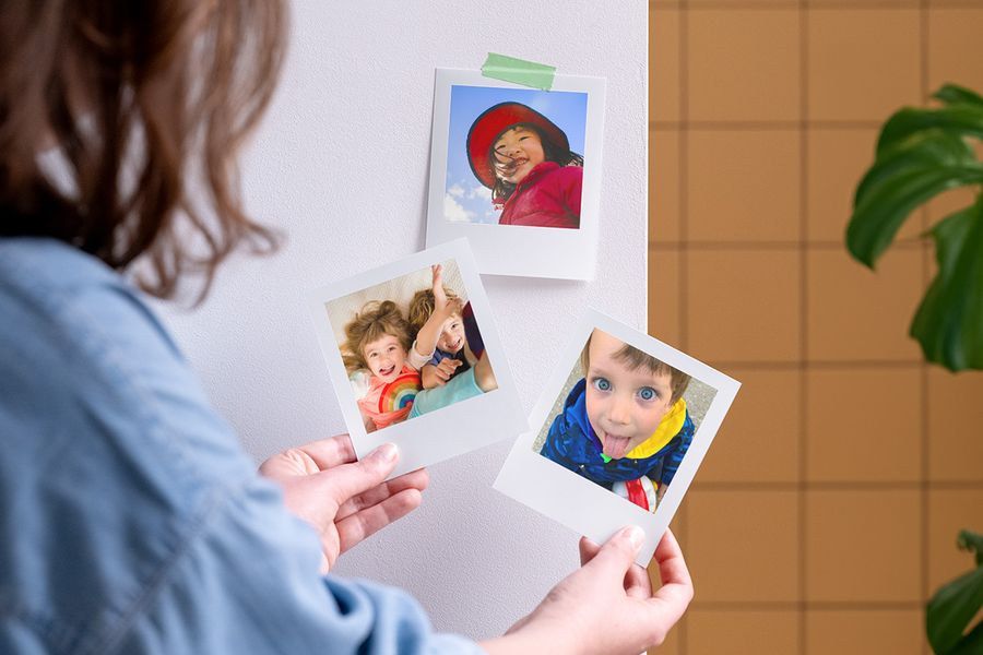Une femme tient des tirages photo personnalisés Photobox, pour inspirer un cadeau fête anniversaire enfant et de petites attentions pour les invités.