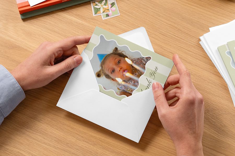 Des mains glissent une carte de remerciement personnalisée pour enfant dans une enveloppe, pour inspirer Photobox et une jolie attention après une fête d’anniversaire enfant.