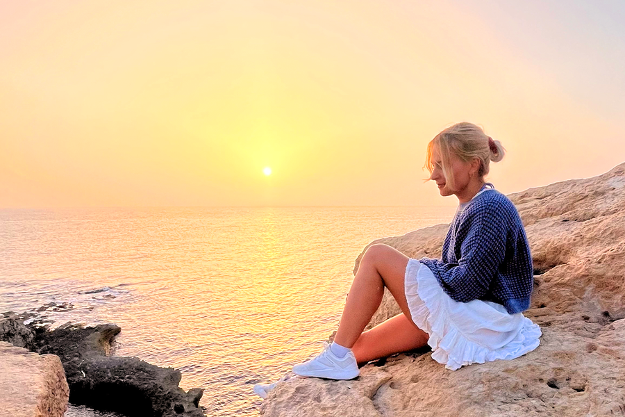 Une femme assise sur des rochers au bord de la mer, avec le soleil couchant derrière elle, illustrant comment la lumière de l’heure dorée permet de créer des photos chaleureuses et magnifiques.