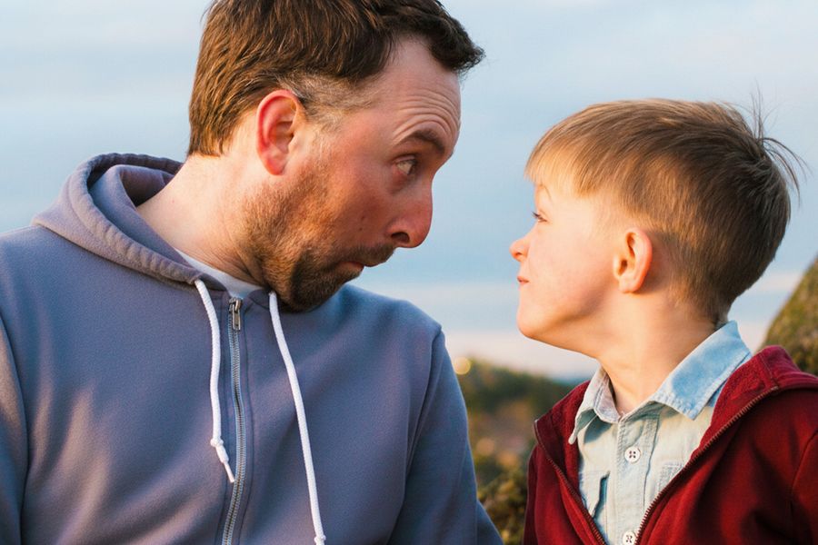 Un père et son fils font des grimaces en se regardant, pour inspirer une carte fête des pères drôle et un message fête des pères plein d’humour.