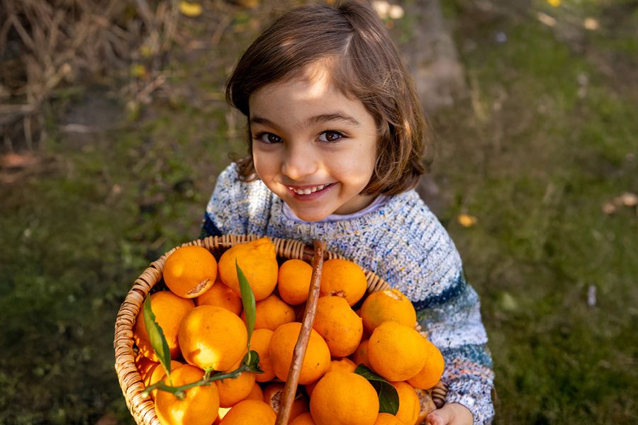 Une jeune fille debout en plein soleil tenant un bol d’oranges, illustrant la difficulté de prendre des photos sous le soleil de midi.