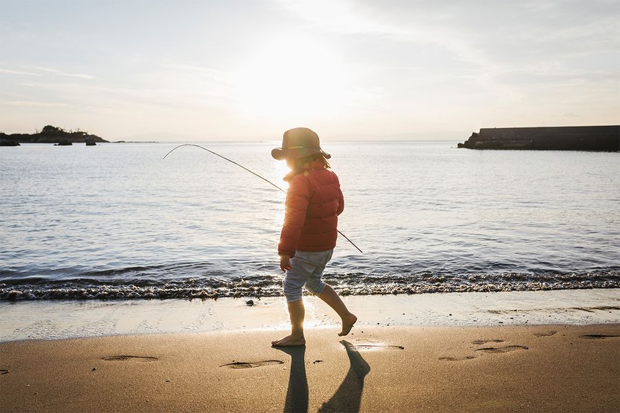 Un enfant debout sur la plage au bord de la mer avec une ombre marquée derrière lui, illustrant l’effet dramatique de la photographie en silhouette au soleil.