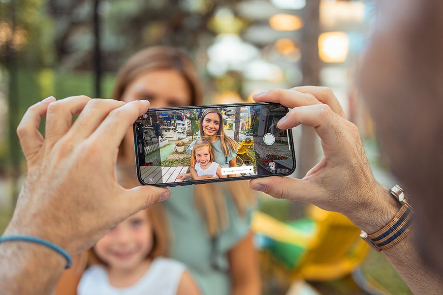 Une main tient un téléphone qui capture une mère souriante et sa fille en plein soleil, illustrant comment prendre des photos en pleine lumière avec son téléphone.