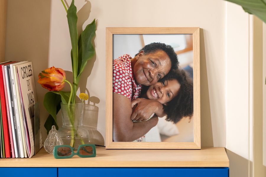 Une photo encadrée d’une grand-mère et de sa petite-fille en train de se serrer dans les bras est posée sur une table à côté de livres, d’un magazine et d’un vase original, pour inspirer des idées d’encadrement et de décoration murale abordable.