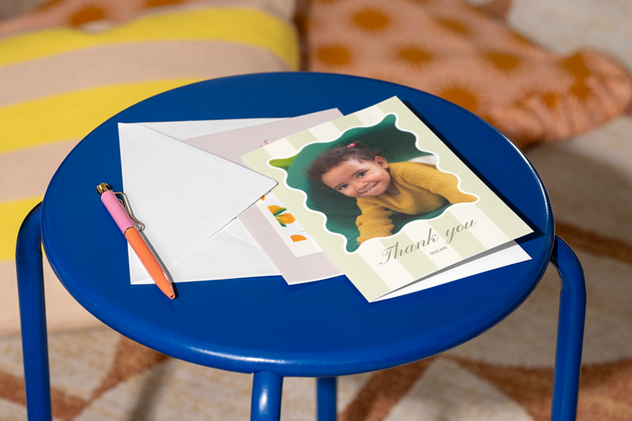 Une carte merci prof personnalisée Photobox avec la photo d’une petite fille sur le devant est posée sur un tabouret avec un stylo à côté, pour inspirer un message de remerciement pour prof à la fois chaleureux et respectueux.