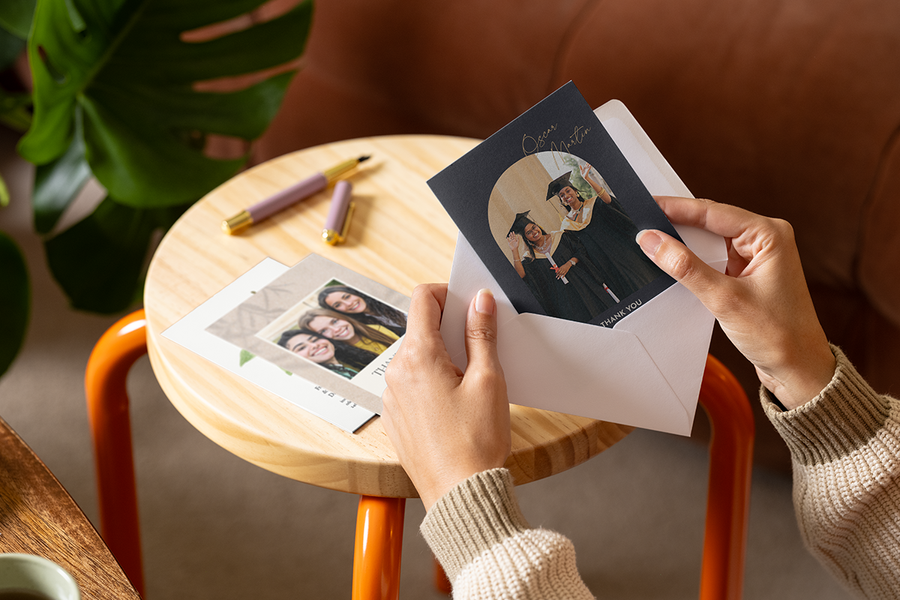 Des mains glissent une carte de remerciement personnalisée Photobox pour enseignant, avec des diplômés sur le devant, dans une enveloppe.