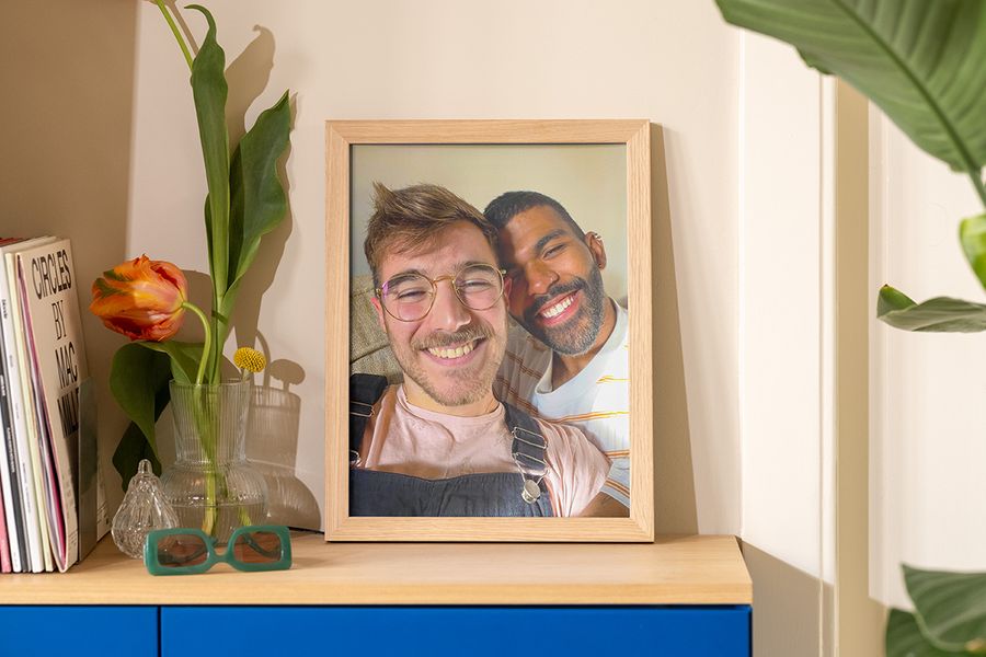 Une photo encadrée de deux hommes prenant un selfie au soleil est posée sur un buffet à côté d’un vase, de lunettes de soleil et d’un magazine, pour inspirer une déco été simple et lumineuse.