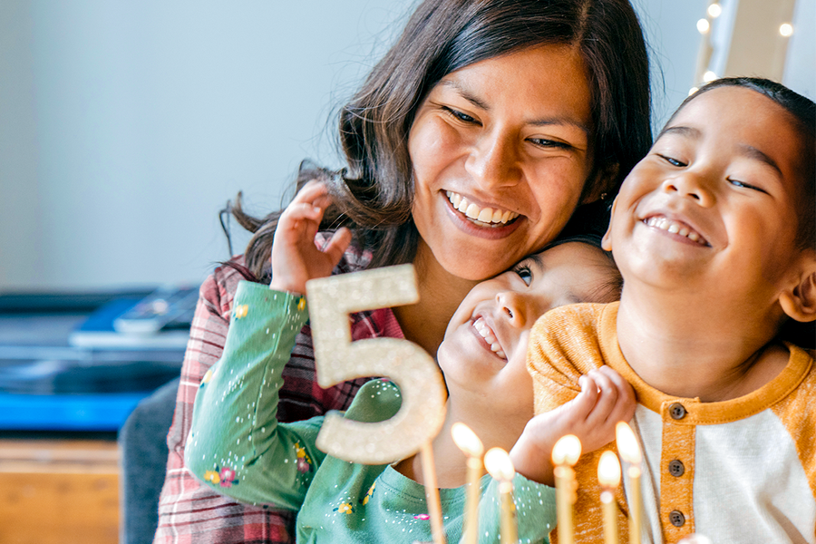 Une mère et ses deux enfants souriant à côté d'un gâteau de 5ème anniversaire, illustrant un cadeau anniversaire maman original de Photobox.