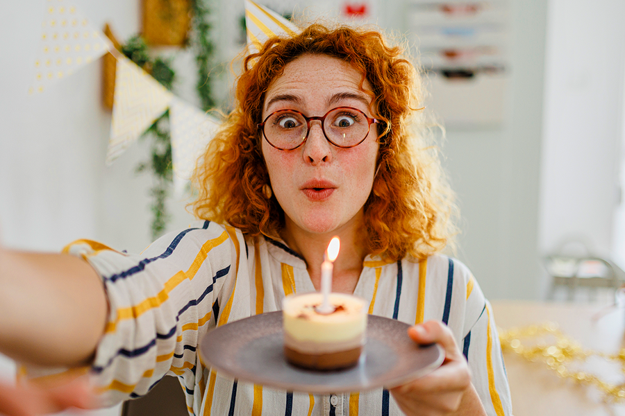 Une femme aux cheveux roux et bouclés tient un cupcake avec une bougie, illustrant des idées de message d’anniversaire pour un collègue et des cartes d’anniversaire Photobox.