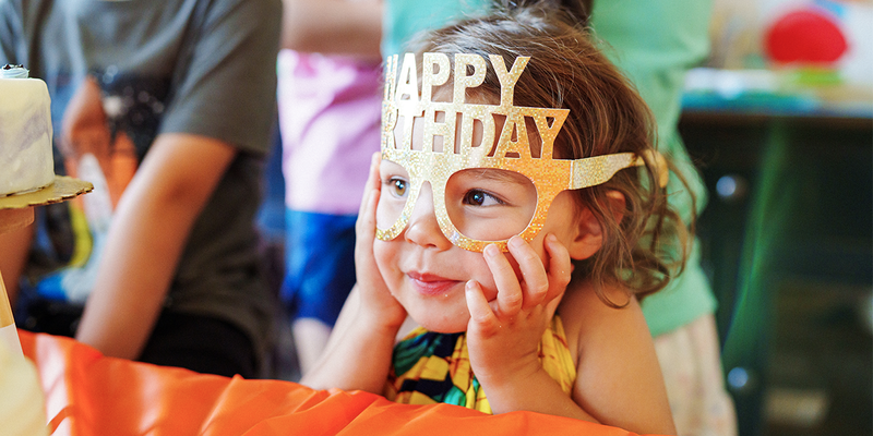 Une petite fille portant des lunettes de fête Joyeux Anniversaire, parfaite pour trouver une idée cadeau anniversaire ou un cadeau anniversaire original chez Photobox.