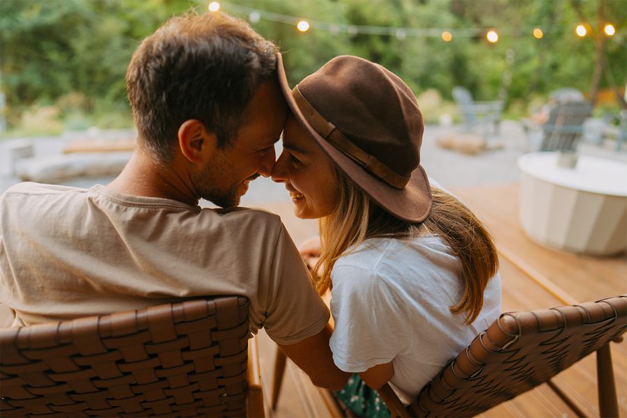 Un homme et une femme se câlinent, assis dans un jardin orné de guirlandes lumineuses, un moment romantique tiré des idées de vacances à la maison pour les couples de Photobox.